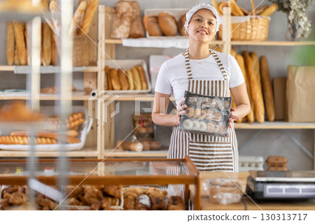 Middle-aged saleswoman holds cookie box in bakery Middle-aged saleswoman holds cookie box in bakery 130313717