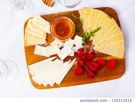 Slices of artisanal cheeses on wooden board with raspberries and honey 130313818
