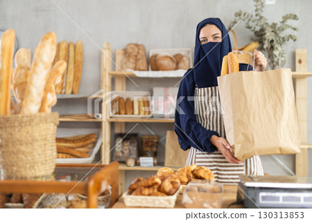 Female bakery owner in niqab holding out paper bag 130313853