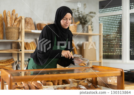 Girl seller of an oriental bakery in traditional muslim clothes with fresh hot croissants in hands 130313864