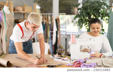 Asian seamstress sews on a machine next to a male fashion designer Asian seamstress sews on a machine next to a male fashion designer 130313865