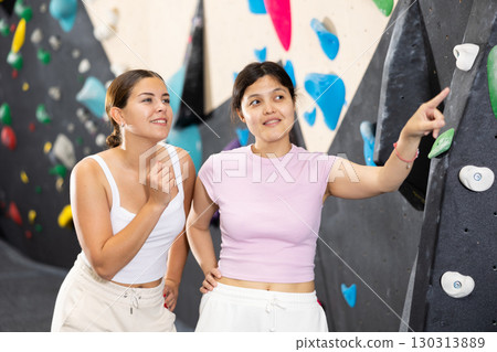 .Women are standing in gym and discussing possible options for overcoming difficult climbing route 130313889