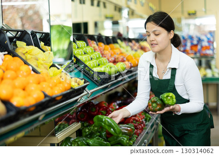 Positive asian girl seller in an apron offers green bell peppers Positive asian girl seller in an apron offers green bell peppers 130314062