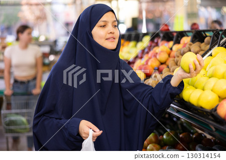 Young asian woman in hijab chooses quality juicy ripe apples Young asian woman in hijab chooses quality juicy ripe apples 130314154