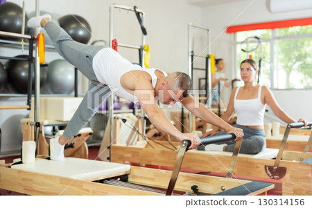 Young guy doing full body exercises lying on reformer device 130314156