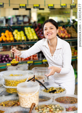 Young woman shopper picking olives in supermarket Young woman shopper picking olives in supermarket 130314177