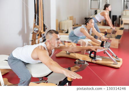 Sportive young guy training her arms turning handle of exercise machine Sportive young guy training her arms turning handle of exercise machine 130314246