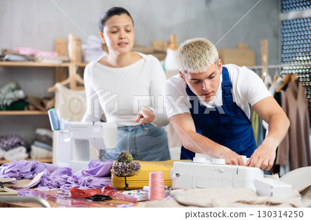 Focused young repairman repairing sewing-machine and Asian tailoress talking 130314250
