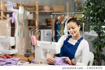 Repairwoman master is collecting and testing sewing machine after repairing sitting at table in sewing workshop 130314255