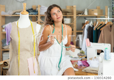 Dreaming female fashion designer sitting on table in sewing studio 130314260