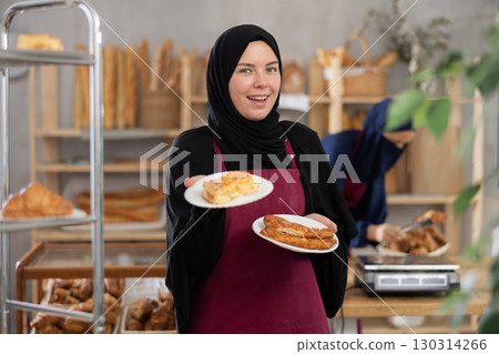 Smiling Muslim saleswoman presenting fresh pastries in bakery 130314266