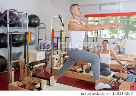 Sportive young guy training her arms and legs on reformer device 130314267
