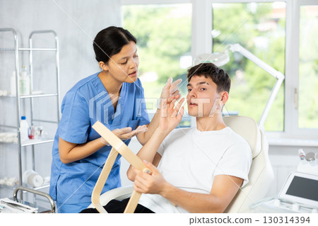 Young cosmetologist woman examining face of young man 130314394