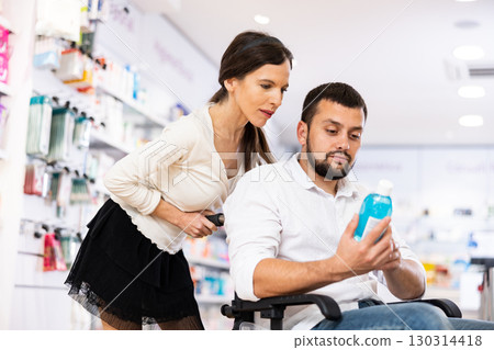 Courteous woman helping man in a wheelchair to choose the right medicine in pharmacy Courteous woman helping man in a wheelchair to choose the right medicine in pharmacy 130314418