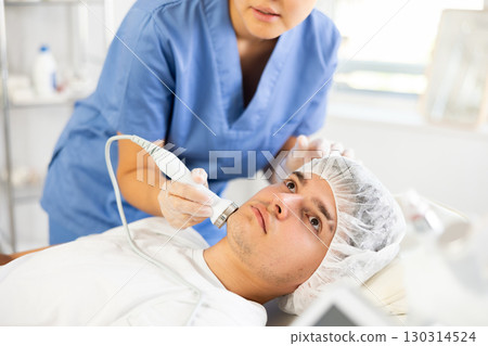 Young woman cosmetologist doing ultrasound procedure to young man 130314524