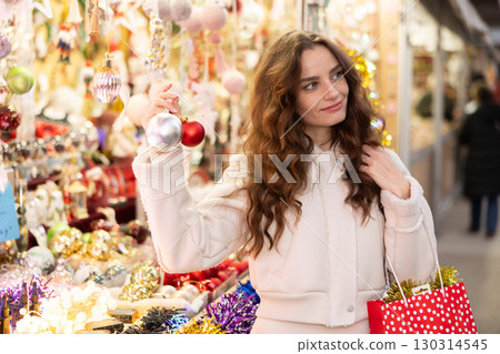 Happy woman holding Christmas baubles while walking through holiday fair Happy woman holding Christmas baubles while walking through holiday fair 130314545
