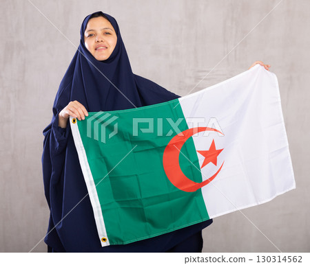 Young Muslim woman in blue hijab holds unfurled flag of Algeria. Young Muslim woman in blue hijab holds unfurled flag of Algeria. 130314562
