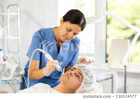 Young woman cosmetologist doing moisturizing procedure to young man 130314577