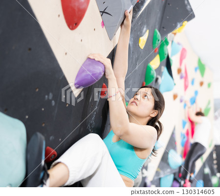 Young Asian woman climbs steep artificial wall in sports complex and trains endurance Young Asian woman climbs steep artificial wall in sports complex and trains endurance 130314605