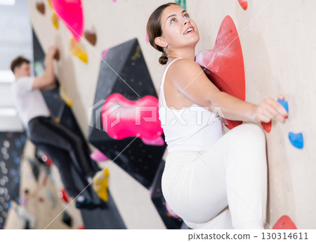 Young Europian woman climbs steep artificial wall in sports complex and trains endurance Young Europian woman climbs steep artificial wall in sports complex and trains endurance 130314611
