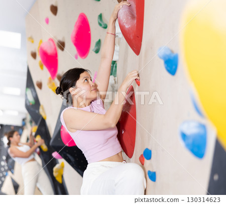 Young Asian woman climbs steep artificial wall in sports complex and trains endurance Young Asian woman climbs steep artificial wall in sports complex and trains endurance 130314623