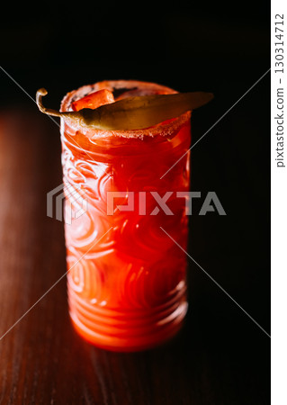 Vegetable cocktail. Spicy beverage. Tomato juice drink served with chili pepper pod. Garnished red alcoholic liquid glass on dark background. 130314712