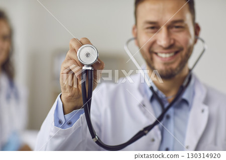 Portrait of a young happy smiling doctor in medical uniform standing with stethoscope in clinic. 130314920