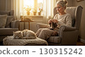 Senior woman knitting at home in a cozy living room with natural light and warm blanket, cat sleeping nearby. 130315242
