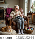 Senior woman knitting at home in a cozy living room with natural light and warm blanket, cat sleeping nearby. 130315244