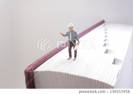 Miniature Engineer Standing On a Large Book Representing Knowledge 130315456