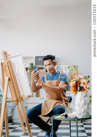 Asian male painter do artwork in art workshop, painting supplies, oil pastels, two canvas easel, creative space with paintbrush 130315819