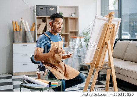 Asian male painter do artwork in art workshop, painting supplies, oil pastels, two canvas easel, creative space with paintbrush Asian male painter do artwork in art workshop, painting supplies, oil pastels, two canvas easel, creative space with paintbrush 130315820
