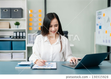 Asian businesswoman working with working notepad, tablet and laptop documents talking on the smartphone, tablet and laptop video call tax 130315928