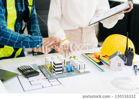 Two colleagues discussing data working and tablet, laptop with architectural project at construction site at desk 130316332