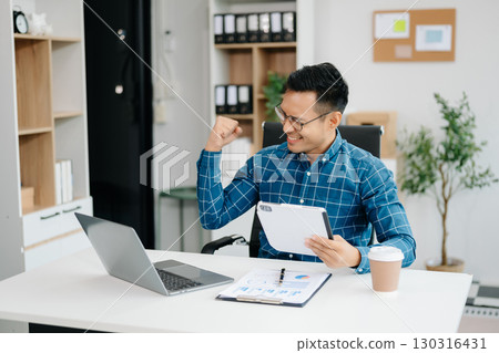 Young handsome man typing on tablet and laptop while sitting at the working table office 130316431
