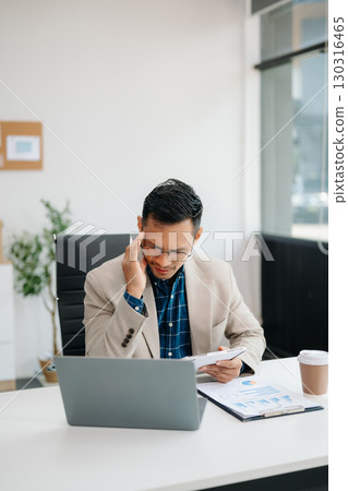 Young handsome man typing on tablet and laptop while sitting at the working table office Young handsome man typing on tablet and laptop while sitting at the working table office 130316465