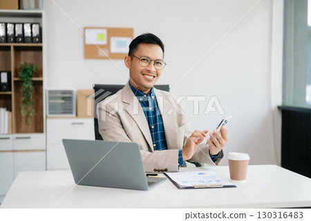 Young handsome man typing on tablet and laptop while sitting at the working table office 130316483