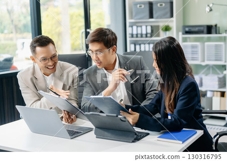 Happy Asian businesspeople while collaborating on a new project.  using a laptop and tablet 130316795