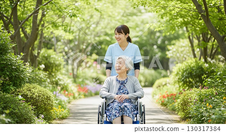 A young nurse happily pushes an elderly woman in a wheelchair through the fresh greenery 130317384