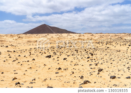 A vast desert landscape on La Graciosa, Lanzarote, featuring a distant volcanic mountain under a bright blue sky. 130319335