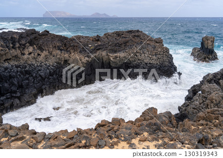 Waves crashing against rugged black volcanic rocks along the coast of La Graciosa, Lanzarote, with a view of the sea. Waves crashing against rugged black volcanic rocks along the coast of La Graciosa, Lanzarote, with a view of the sea. 130319343