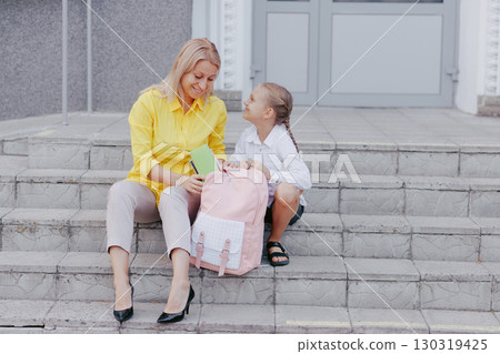 Mother helps daughter organize backpack on school steps for back to school morning showing support and happiness. Mother helps daughter organize backpack on school steps for back to school morning showing support and happiness. 130319425