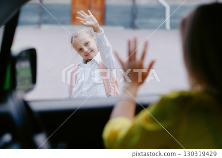 Young girl waves goodbye to her parent before school, capturing an emotional back to school morning and family support. 130319429