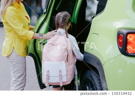 Mother helps daughter get into car for the school run, showing family support, safety, and back to school morning routine. 130319432