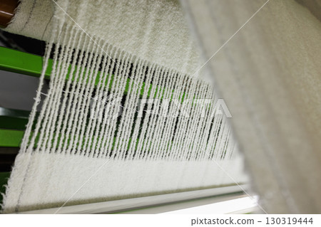 Woolen fabric weaving in progress on an industrial loom, showcasing textile production and manufacturing process closeup. 130319444