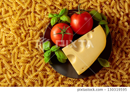 Uncooked fusilli pasta with tomatoes, basil and cheese. 130319595