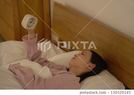 A woman looking at the clock in her futon late at night A woman looking at the clock in her futon late at night 130320183
