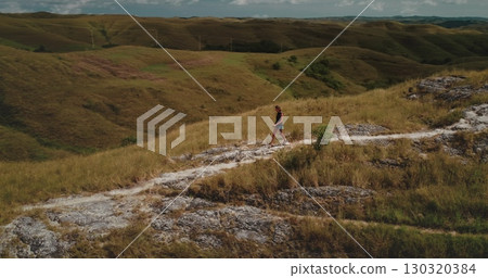 Tourist walking along a scenic path in the Sumba hills of Indonesia, soaking in the breathtaking landscape on a sunny day while enjoying a refreshing hike through the wilderness 130320384