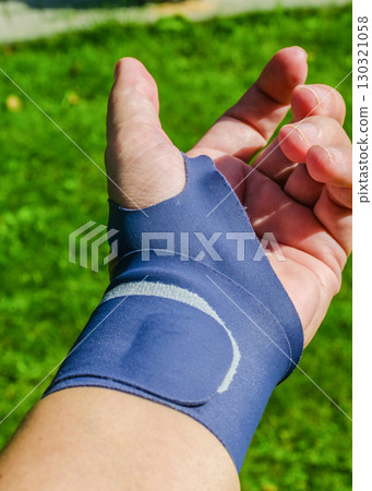 A detailed view of a human hand with a blue orthopedic wrist brace for joint support, photographed on a green grass background . High quality photo A detailed view of a human hand with a blue orthopedic wrist brace for joint support, photographed on a green grass background . High quality photo 130321058