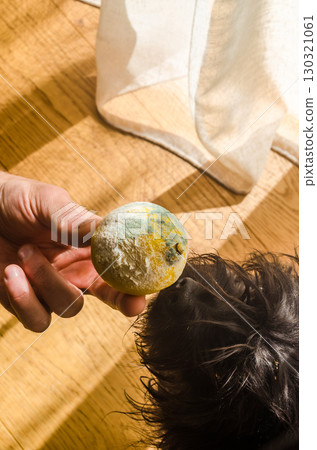 A hand holds a moldy lemon with green and white fungus near a curious dog indoors. Concept of spoiled food, food safety, and household waste. High quality photo A hand holds a moldy lemon with green and white fungus near a curious dog indoors. Concept of spoiled food, food safety, and household waste. High quality photo 130321061
